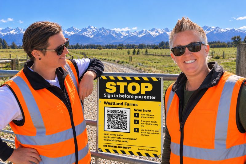 Jane and Charli in hi-vis vests at a farm gate with an EverAccess sign, the Southern Alps behind them